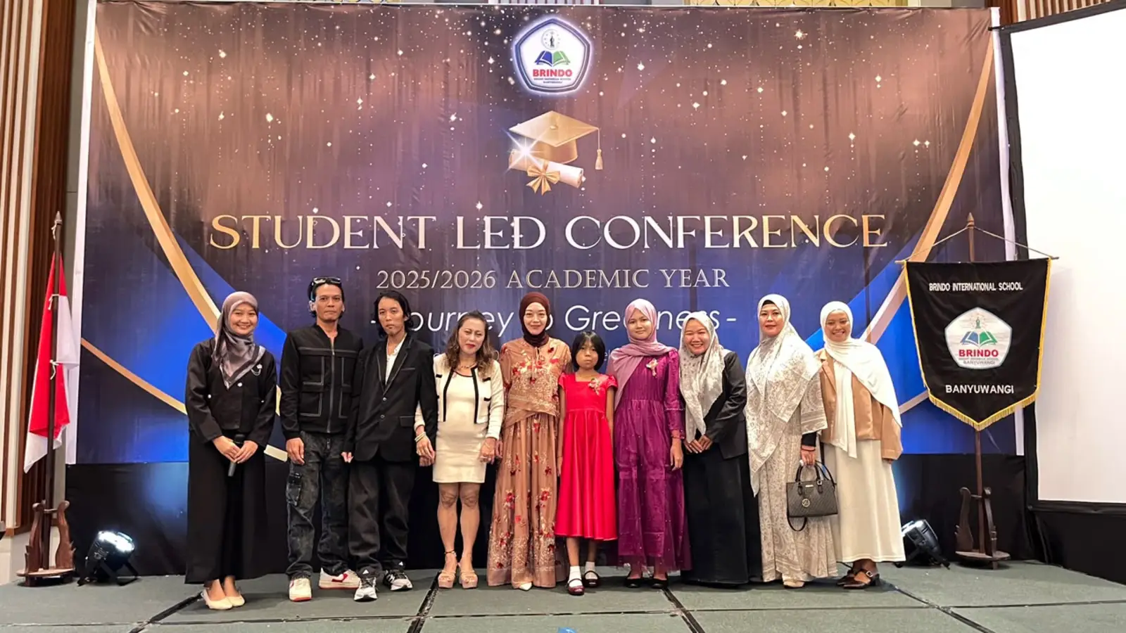 Primary School graduates pose with their parents and teachers on the Student Led Conference 2025/2026 stage at Kokoon Hotel, Banyuwangi.